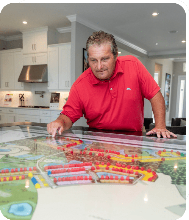 Man in red shirt pointing at a colorful model layout on a table.