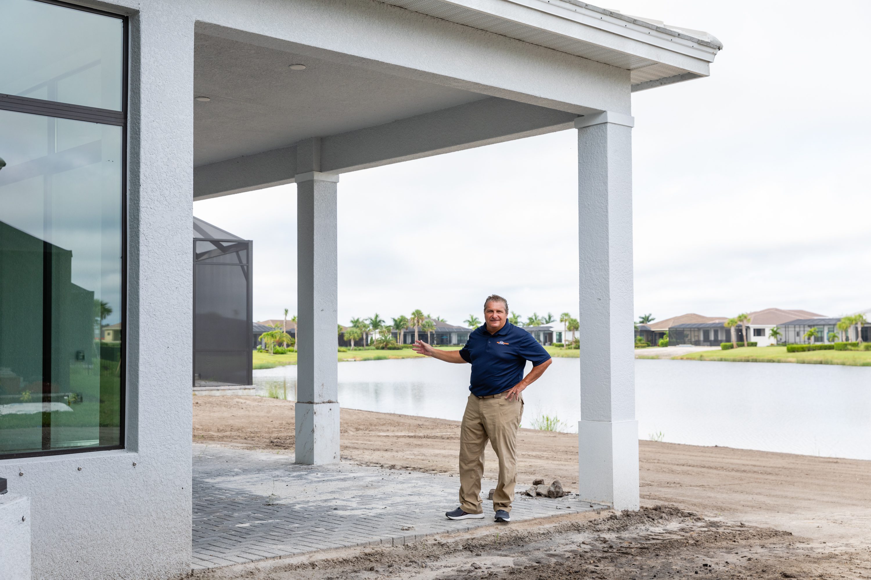 Man standing under a porch roof next to a lake in a residential area.