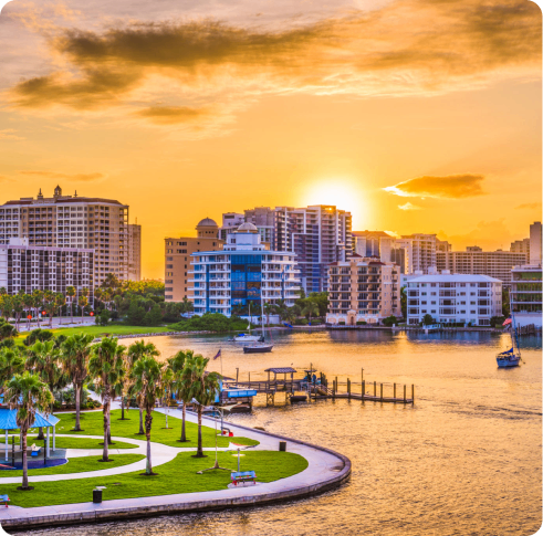Sunset over a waterfront cityscape with boats and palm trees.